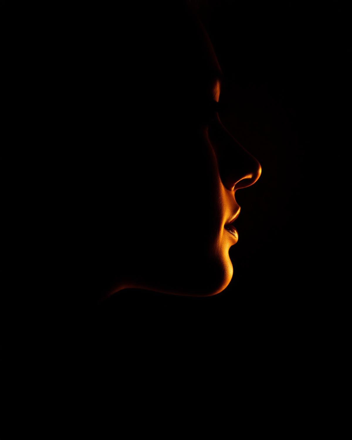 Perfil facial iluminado con luz cálida sobre fondo oscuro